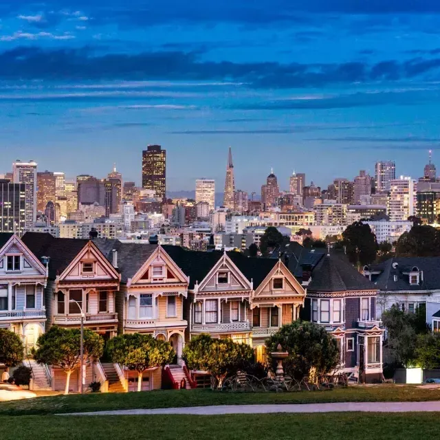 夕暮れのサンフランシスコのスカイラインを背景に、有名なアラモ・スクエアのペインテッド・レディが描かれています。